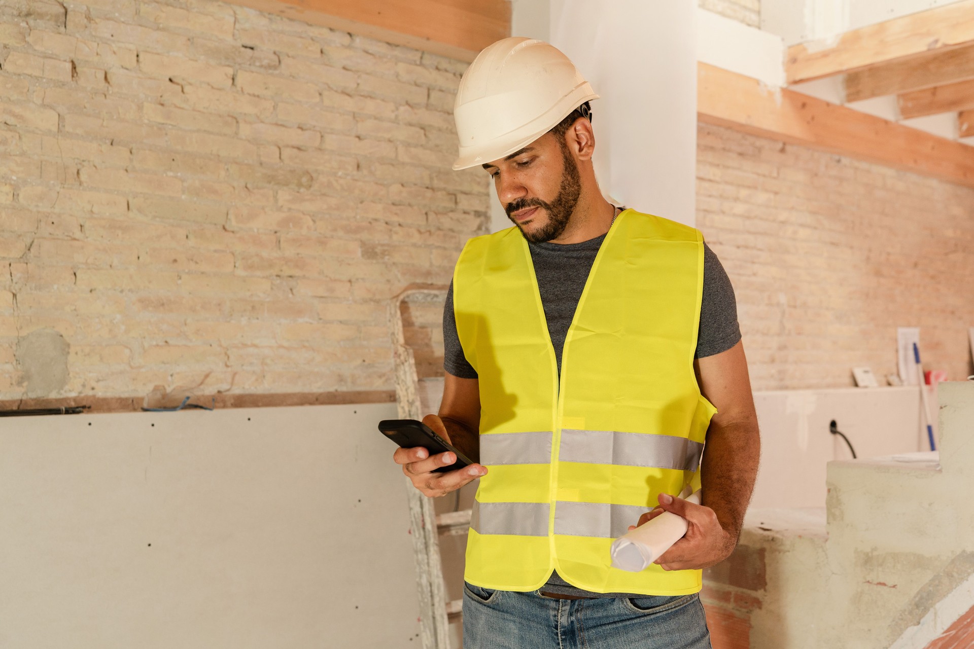 Male Contractor wearing hardhat and safety vest using smartphone on construction site